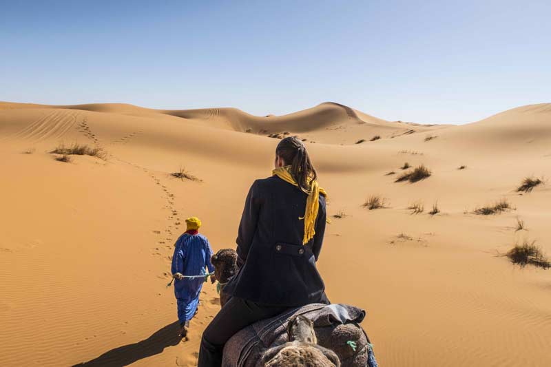 Berber führt eine Frau auf einem Kamel durch die Sahara