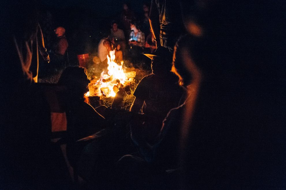 Personen sitzen nachts um ein Lagerfeuer