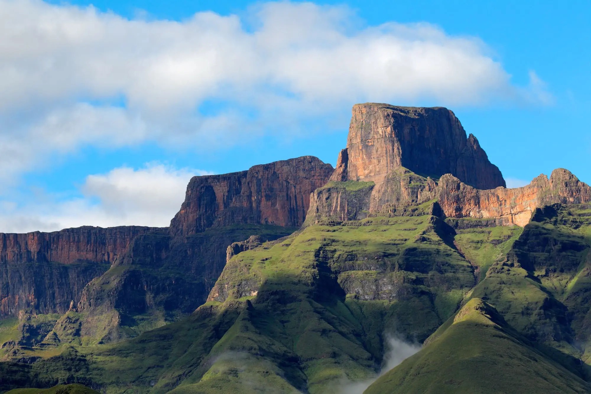 Majestätische Berglandschaft mit steilen Klippen, üppigem Grün und klarem Himmel.