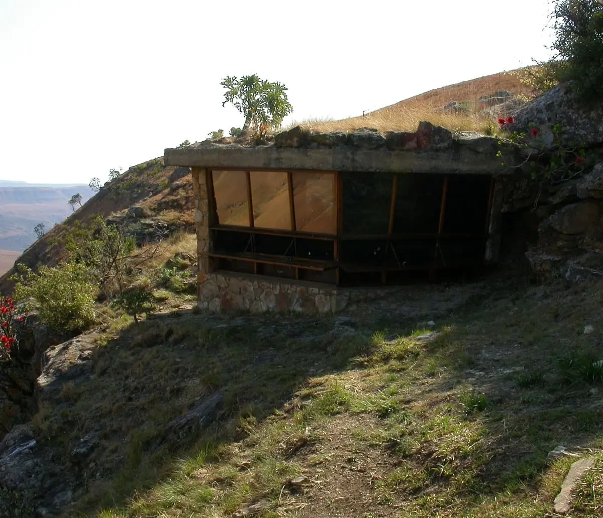 Steinhaus in hügeliger Landschaft mit Gras und Bäumen, eingebaut in einen Hang, mit Aussicht ins Tal.