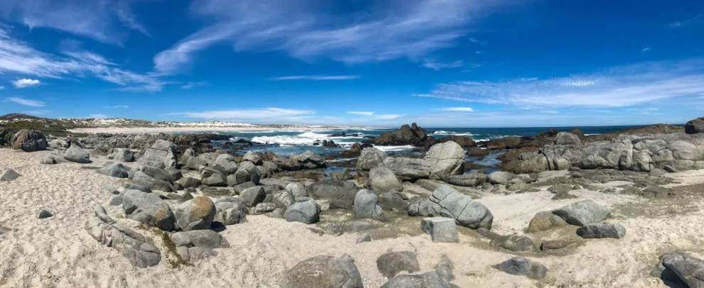 Steiniger Strand unter blauem Himmel, Wellen brechen sanft an der felsigen Küste. Perfekte Kulisse für Naturfreunde.